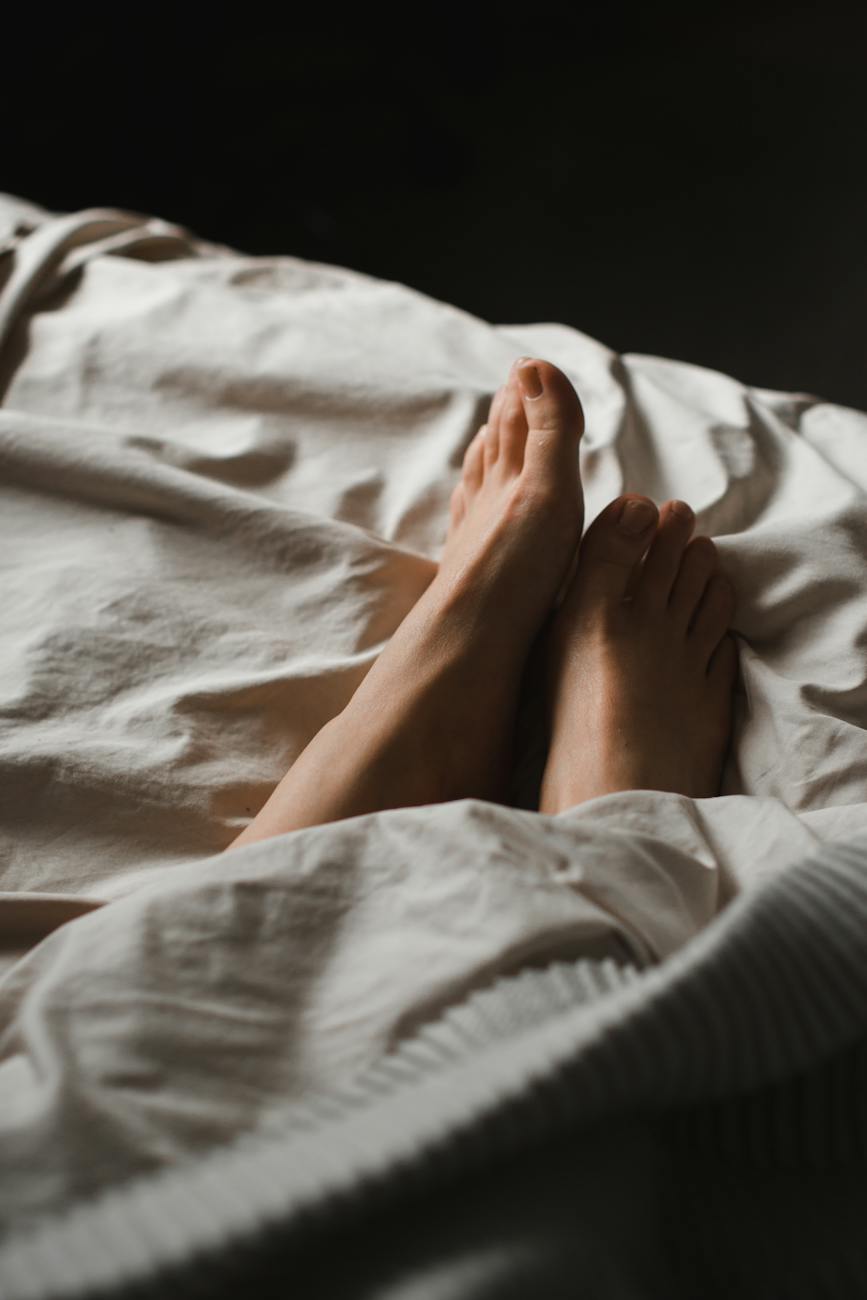 crop unrecognizable female feet lying in cozy bed